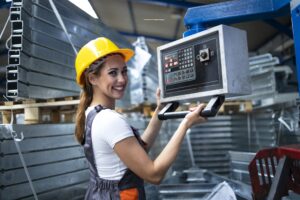 Arbeiterin mit gelbem Helm steht an CNC-Steuerung